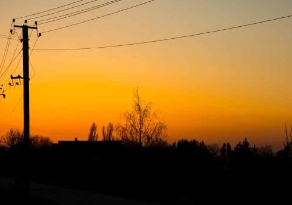 Beautifull yellow summer sunset sunset against the background village , building , trees and electricity power lines , electric pillars